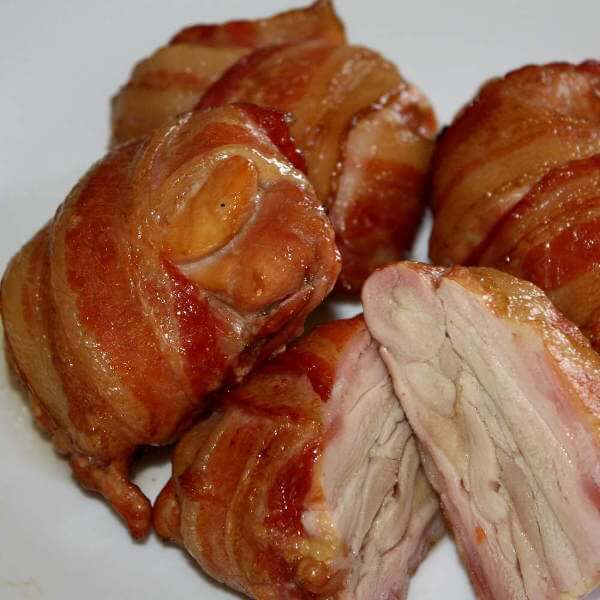Bacon Wrapped Boneless, Skinless Chicken Thighs, Served On a Plate, One Cut In Half To Show Its Inner Beauty