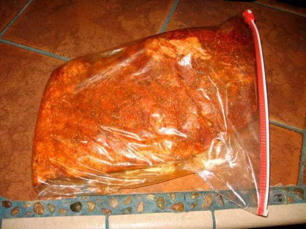 A brisket seasoned with aromatic spices is inside a sealed, gallon size food storage bag, left to marinate in the flavorful rub.