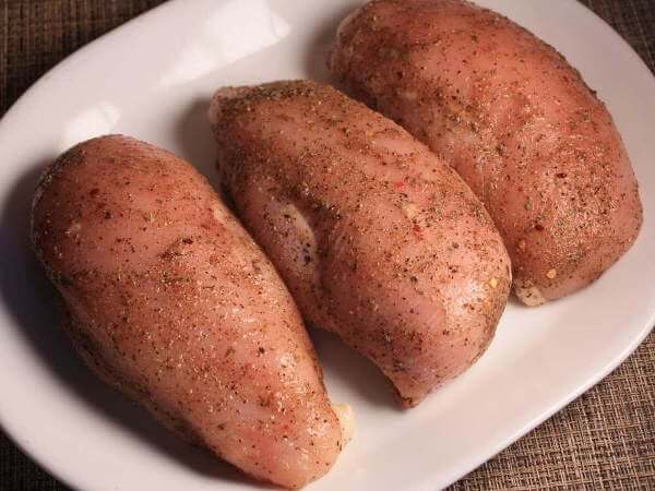 Three Raw, Seasoned, Boneless Skinless Chicken Breasts on White Platter