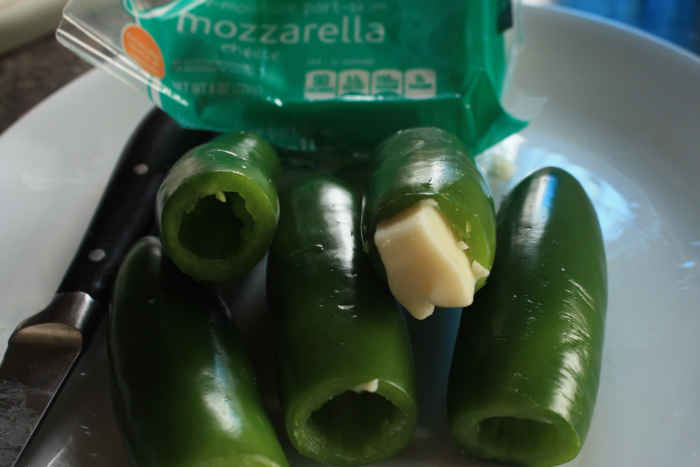 When stuffing the peppers, be gentle. The walls of the jalapenos can crack if too much goodness is stuffed inside! Cored jalapeno peppers, one of them already filled with a small chunk of Monterrey Jack cheese.