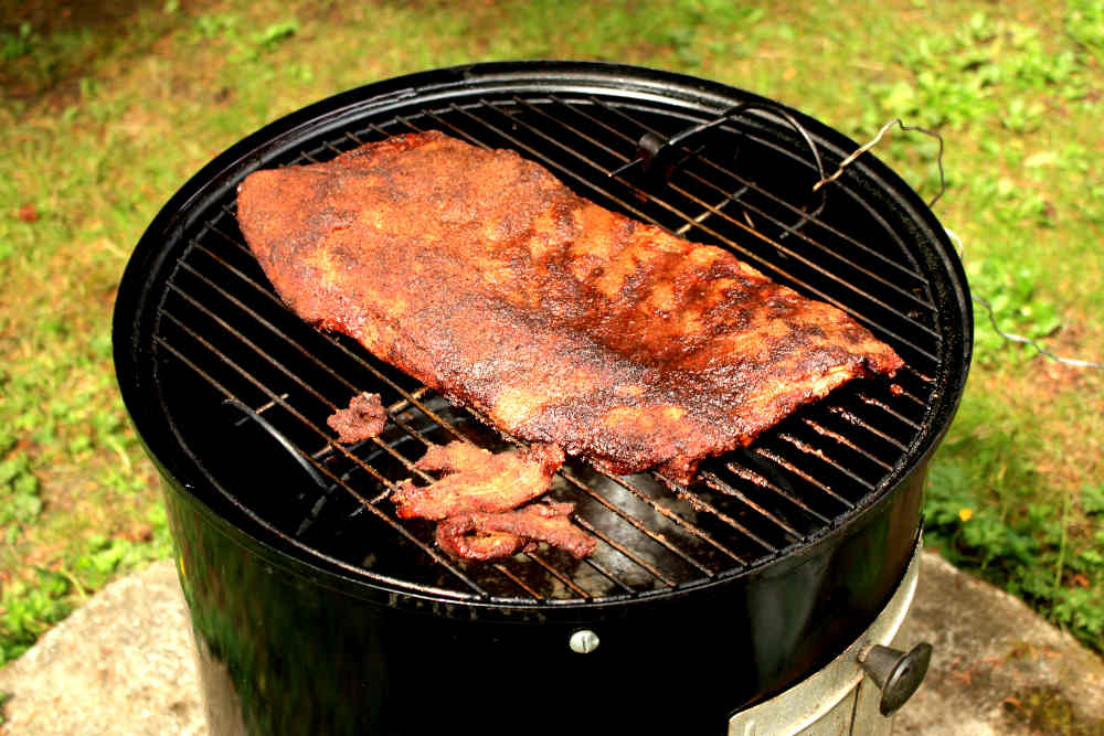 Spare ribs slab cooking on the top grate of a Weber Smoky Mountain Cooker. Pin to save