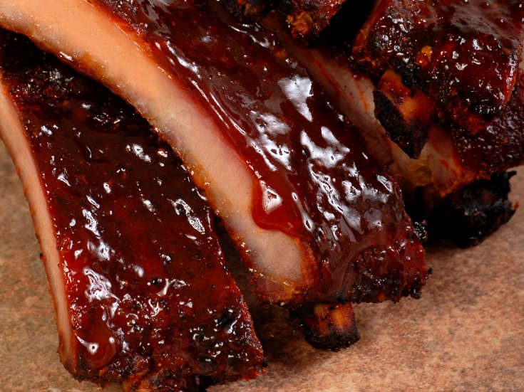 Red BBQ sauce coating a pile of smoked spare ribs