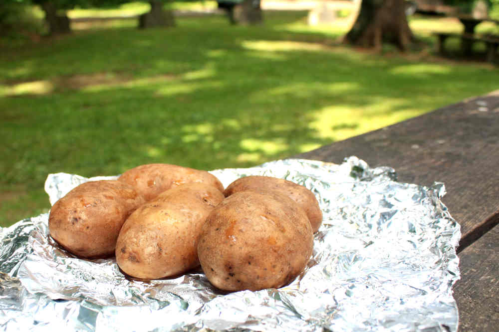 Russet potatoes on a crumpled section of aluminum foil, opened up after partially cooking them in the smoker.