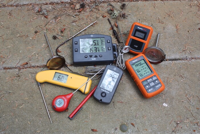 A variety of single and dual probe cooking thermometers on a picnic table.