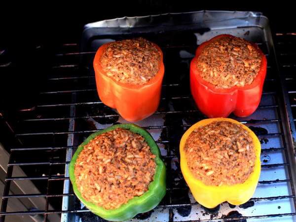 Red, Orange, Yellow And Green Sweet Peppers, Stuffed With Beef, On a Meat Smoker Rack Four Uncooked Stuffed Peppers, Just Placed Into The Char-Broil Propane Smoker