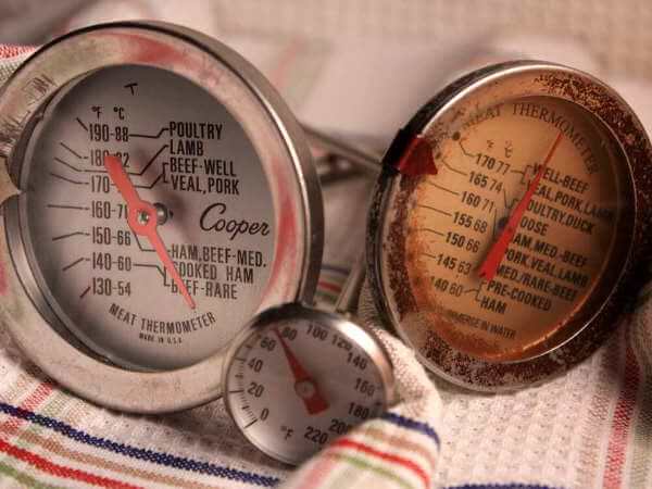 Three Analog Dial Smoker and Meat Thermometers Resting On a Patterned Dish Towel